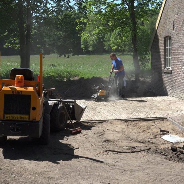 Robert en Kees leggen een terras voor de schuur.